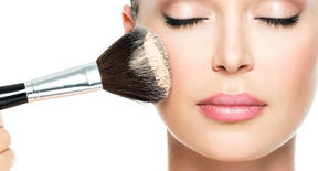 Closeup portrait of a woman  applying dry cosmetic tonal foundation  on the face using makeup brush.